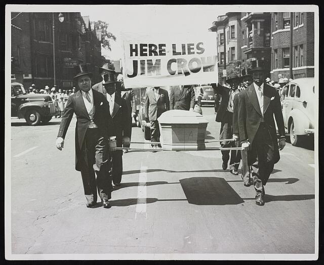 [Pallbearers with casket walking in front of sign reading "here lies Jim Crow" during the NAACP Detroit branch "Parade for Victory"]